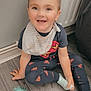 Corey joined the competition — help win amazing prizes! bib, child, cute, floor, happy, home, indoor, pajamas, person, playful, radiator, short_hair, sitting, smiling, sock, superman_logo, toddler, toy, wooden_floor, young_child