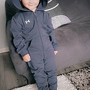 Corey joined the competition — help win amazing prizes! child, hoodie, jumpsuit, smile, indoor, rug, carpet, couch, pillow, floor, wood_floor, person, young_child, cozy, casual_clothing, standing, home, furniture, soft_lighting, portrait