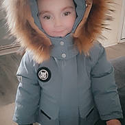 Corey joined the competition — help win amazing prizes! child, winter_coat, hood, fur_trim, indoor, smile, standing, jacket, young, clothing, person, face, warm, cute, pants, hand, floor, home, casual, portrait