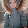 child, winter_coat, hood, fur_trim, indoor, smile, standing, jacket, young, clothing, person, face, warm, cute, pants, hand, floor, home, casual, portrait