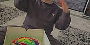 Corey is registered to the contest to win money with this photo: birthday, box, cake, carpet, celebration, child, cute, dinosaur, floor, happy, home, indoor, living_room, person, shoes, smile, sweatshirt, toddler, toy, young