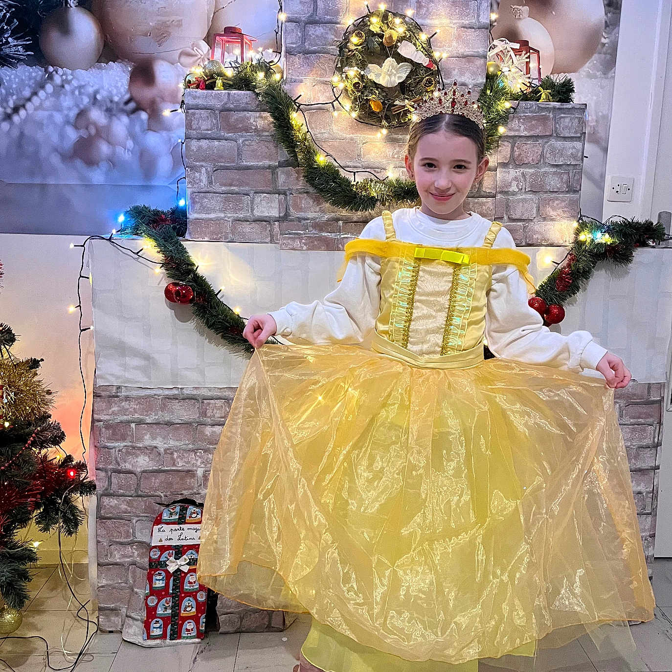 Lyse participe au concours pour gagner de l'argent avec cette photo : child, girl, princess, dress, yellow_dress, crown, smile, holiday, christmas, decorations, lights, garland, fireplace, indoor, floor, boots, pose, festive, celebration, portrait