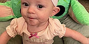 Winter is registered to the contest to win money with this photo: baby, child, headband, pink_bow, plush_chair, green, toy, indoor, clothing, cute, smile, face, person, infant, earrings, carpet, background, sitting, baby_gear, candid