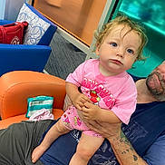 Sophia joined the competition — help win amazing prizes! toddler, child, person, curly_hair, pink_clothing, sitting, adult, tattoo, orange_chair, blue_chair, indoor, window, hand, shorts, facial_expression, hair, skin, floor, bag, cushion