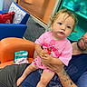 adult, bag, blue_chair, child, curly_hair, cushion, facial_expression, floor, hair, hand, indoor, orange_chair, person, pink_clothing, shorts, sitting, skin, tattoo, toddler, window