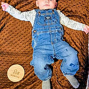 Kaspian joined the competition — help win amazing prizes! arms_outstretched, baby, brown_blanket, casual, child, clothing, cute, denim_overalls, dinosaur_print, face, indoor, infant, long_sleeve_shirt, lying_down, portrait, six_months, socks, soft_blanket, texture, wooden_sign
