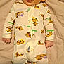 baby, infant, smiling, onesie, dog_pattern, blanket, cute, tongue_out, sleepwear, lying_down, child, soft_texture, happy, young_child, indoors, person, portrait, face, cozy, sleeping_area