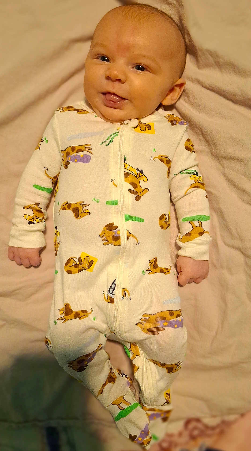 Kaspian joined the competition — help win amazing prizes! baby, infant, smiling, onesie, dog_pattern, blanket, cute, tongue_out, sleepwear, lying_down, child, soft_texture, happy, young_child, indoors, person, portrait, face, cozy, sleeping_area