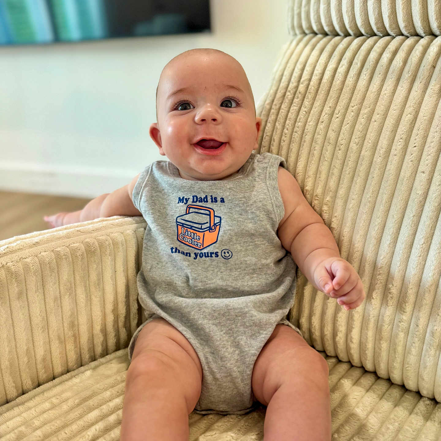 Amir is registered to the contest to win money with this photo: baby, child, infant, smiling, happy, portrait, sitting, armchair, furniture, home, indoor, onesie, clothing, bare_legs, socks, face, eyes, short_hair, cozy, text_on_clothing