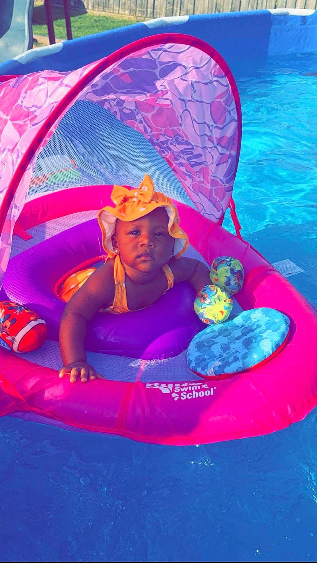 Soraya joined the competition — help win amazing prizes! baby, child, pool, float, floatie, water, swim, sunhat, orange_hat, pink_float, purple_cushion, toy, outdoor, summer, sunny, fence, grass, swimming_pool, infant, relaxing