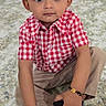 toddler, child, boy, blue_eyes, curly_hair, red_checkered_shirt, beige_pants, bracelet, shoe, sitting, indoor, carpet, portrait, cute, young_child, expression, hands, footwear, floor, home