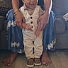 Zixton is registered to the contest to win money with this photo: baby, child, adult, woman, glasses, smiling, standing, supporting_hands, couch, living_room, floor, footwear, vest, pants, barefoot, fabric, home_interior, person, happy, casual_clothing