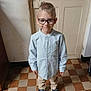 child, boy, glasses, shirt, pants, shoes, standing, indoor, floor, door, smile, portrait, young, person, casual_clothing, light, window_light, happy, home, checkered_floor