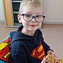 child, boy, glasses, superman_hoodie, cookie, smile, coloring_page, crayon, table, indoor, cabinet, chair, happy, face, person, clothing, furniture, drawing, art, seated