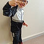 child, boy, glasses, smiling, peace_sign, tracksuit, sportswear, indoor, standing, floor, wall, red_shoes, black_pants, white_jacket, happy, casual, portrait, person, footwear, young