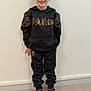 child, boy, glasses, smiling, standing, indoor, black_clothing, hoodie, pants, sneakers, wall, floor, casual_wear, young, happy, portrait, feet, fashion, person, standing_pose