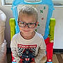 child, boy, glasses, smile, action_figure, captain_america, toy, easel, window, indoor, shirt, long_sleeve, white_shirt, floor, furniture, playroom, happy, person, portrait, casual