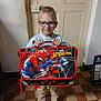 child, boy, glasses, spiderman, bag, indoor, floor, door, smile, standing, blue_shoes, casual_clothing, tiled_floor, backpack, superhero, marvel, young, person, happy, holding