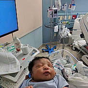 Jordan is registered to the contest to win money with this photo: baby, newborn, hospital, medical_equipment, blanket, bed, infant, person, healthcare, monitor, iv_stand, clothing, sleeping, indoors, patient, nursery, curly_hair, hospital_room, care, resting