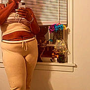 Sage joined the competition — help win amazing prizes! person, cat, mirror_selfie, window, blinds, flowers, vase, beige_clothing, loungewear, reflection, phone, glasses, wood_floor, indoor, curious_cat, hand_on_face, sitting_cat, colorful_flowers, decor, text_overlay