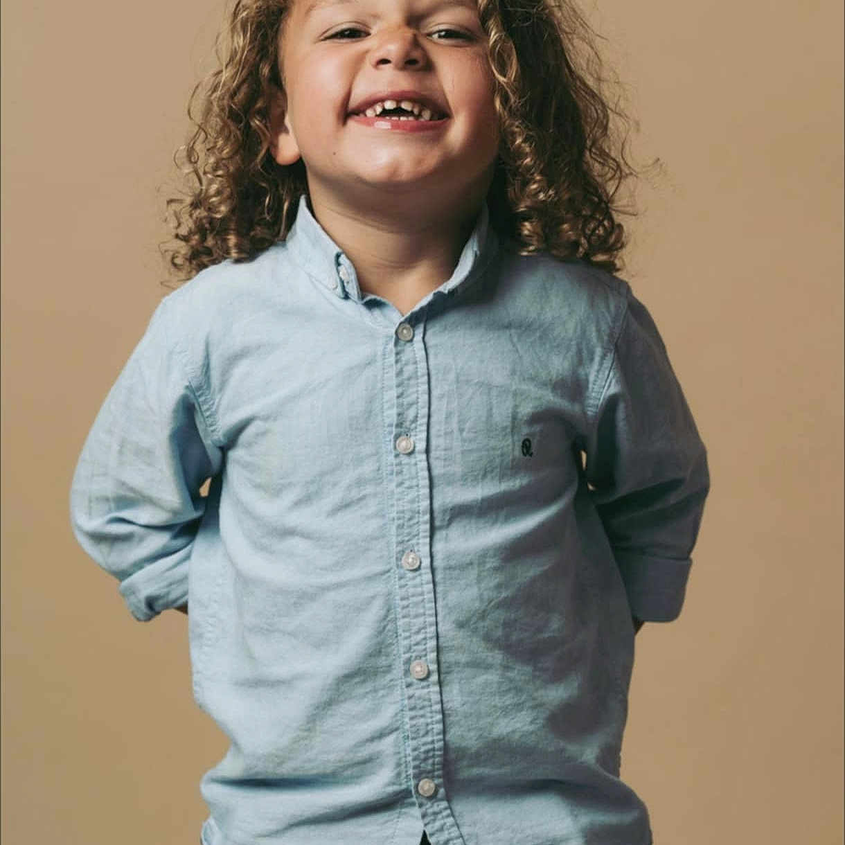 Maïdine a rejoint le concours — aidez-le/la à gagner de superbes lots ! beige_background, blue_shirt, button_up, casual_clothing, child, curly_hair, cute, fashion, gap_tooth, hands_behind_back, happy, jeans, kid, light, long_sleeves, person, portrait, smiling, standing, studio