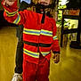 Maïdine a rejoint le concours — aidez-le/la à gagner de superbes lots ! child, firefighter_costume, helmet, peace_sign, curly_hair, indoor, floor, christmas_tree, holiday_decorations, person, adult, shoe, pants, jacket, reflection, smile, happy, toy, lighting, home