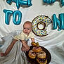 Daniel joined the competition — help win amazing prizes! baby, donuts, balloons, blue, sprinkles, plate, white_background, infant, cute, celebration, food, playful, child, cream_shirt, decorations, sweet_treats, party, smiling, indoor, curious