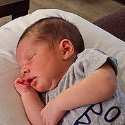 Mark is registered to the contest to win money with this photo: baby, sleeping, infant, child, indoor, gray_shirt, wooden_floor, furniture, peaceful, resting, portrait, person, cute, newborn, soft_surface, hand, head, ear, skin, clothing