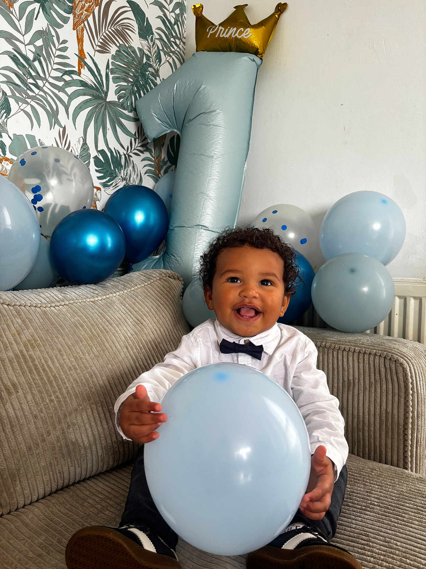 Noah participe au concours pour gagner de l'argent avec cette photo : toddler, balloon, birthday, number_one_balloon, crown_balloon, smiling_child, couch, indoor, party_decorations, bow_tie, white_shirt, happy, celebration, blue_balloons, silver_balloons, curly_hair, child, portrait, home, decor