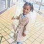 casual, child, clothing, curly_hair, daylight, fashion, happy, outdoor, person, portrait, rainy, sidewalk, smiling, sneakers, street, toddler, trench_coat, umbrella, urban, wet_tiles