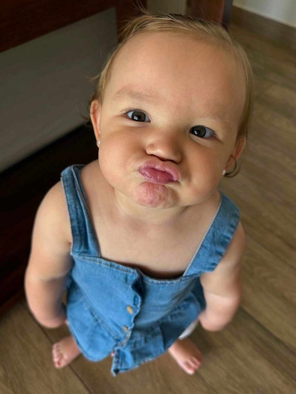 Valentina is registered to the contest to win money with this photo: toddler, child, denim_dress, barefoot, puckered_lips, looking_up, indoor, wooden_floor, cute, baby, portrait, smiling, person, face, skin, short_hair, earrings, standing, young_child, playful