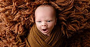 Caden is registered to the contest to win money with this photo: baby, blanket, brown, child, close_up, cozy, eyes, face, fluffy, infant, lying_down, newborn, open_mouth, photography, portrait, sleepy, studio, swaddled, textured, wrapped