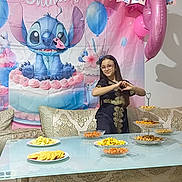 Ainaya participe au concours pour gagner de l'argent avec cette photo : child, girl, birthday, party, balloon, stitch, backdrop, snacks, table, sofa, glasses, dress, hand_gesture, pink, decorations, food, celebration, indoor, smile, young