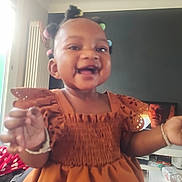 Aliyah a rejoint le concours — aidez-le/la à gagner de superbes lots ! toddler, child, smiling, dress, colorful_hair_beads, indoor, living_room, television, furniture, joyful, hands, portrait, person, cute, happy, black_hair, home, baby, young_child, casual