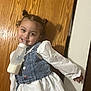 casual, child, clothing, cute, denim_vest, face, fun, girl, hair_buns, happy, indoor, milk_bottle, person, playful, portrait, smile, standing, white_dress, wooden_door, young_child