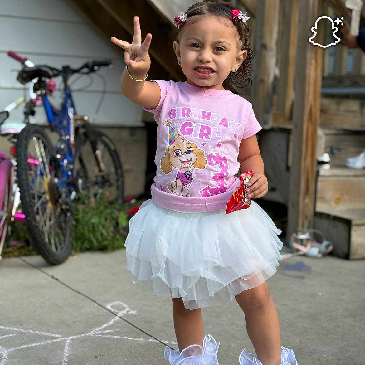Joulisa is registered to the contest to win money with this photo: bicycles, birthday_girl, chalk_drawing, child, concrete, curly_hair, daylight, frilly_socks, hair_bows, happy, holding_snack, outdoor, peace_sign, person, pink_sneakers, pink_tshirt, playful, smiling, stairs, white_tutu