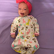 Zoey is registered to the contest to win money with this photo: baby, infant, smiling, headband, bow, onesie, animal_print, monkey_print, giraffe_print, elephant_print, purple_sheet, bed, laying_down, cute, newborn, hands, feet, portrait, happy, fabric