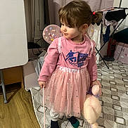 Victoire participe au concours pour gagner de l'argent avec cette photo : toddler, child, indoor, pink_clothing, tutu, plush_toy, fairy_wings, toy_wand, curly_hair, floor_rug, socks, sweatshirt, curious, standing, laundry_rack, curtains, wood_floor, household_items, playful, room