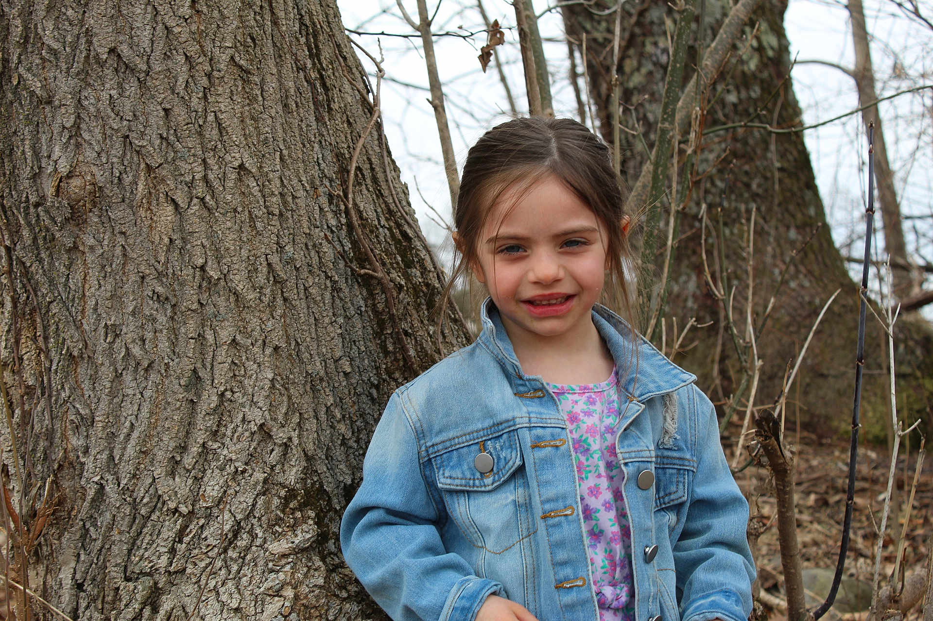 Emma joined the competition — help win amazing prizes! child, girl, denim_jacket, floral_shirt, tree_trunk, outdoor, nature, smile, young, portrait, casual_clothing, spring, brown_hair, standing, background, branches, bark, forest, daylight, person
