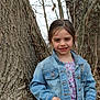 Emma is registered to the contest to win money with this photo: child, girl, denim_jacket, floral_shirt, tree_trunk, outdoor, nature, smile, young, portrait, casual_clothing, spring, brown_hair, standing, background, branches, bark, forest, daylight, person