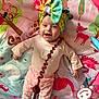 animal_print, baby, bow, child, colorful, cute, expression, face, happy, headwear, indoors, infant, lying_down, patterned_pants, pink_clothing, playmat, playtime, smiling, toddler, toy