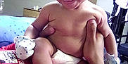 Lia Kalanie Rosalez is registered to the contest to win money with this photo: baby, infant, smile, dimples, mittens, diaper, hand, person, indoor, bed, furniture, shirt, red_clothing, skin, foot, happy, child, room, adult, holding