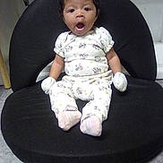 Lia Kalanie Rosalez is registered to the contest to win money with this photo: baby, infant, child, onesie, mittens, sitting, black_cushion, floor, indoor, expression, mouth_open, cute, clothing, person, young_child, hair, face, footwear, sock, surprised