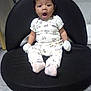 baby, infant, child, onesie, mittens, sitting, black_cushion, floor, indoor, expression, mouth_open, cute, clothing, person, young_child, hair, face, footwear, sock, surprised