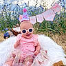 Elena is registered to the contest to win money with this photo: baby, child, outdoor, birthday, party_hat, sunglasses, pink_clothing, flowers, grass, blanket, stuffed_animal, smiling, cute, celebration, nature, sunlight, banner, dress, footwear, happy