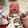 newborn, baby, infant, hospital, nasal_tube, medical_tape, onesie, football_pattern, person, winking, holding, cute, small, human, child, bedroom_furniture, floor, healthcare, caregiver_hand, clothing