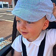 Sébastien participe au concours pour gagner de l'argent avec cette photo : toddler, child, baby, hat, cap, blue_eyes, white_shirt, stroller, safety_straps, outdoor, urban, side_profile, smile, curious, face, person, daylight, street, casual_clothing, headwear