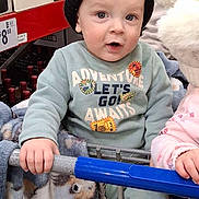 Enzo is registered to the contest to win money with this photo: aisle, baby, blanket, blue, child, clothing, curious, cute, expression, face, green, hand, hat, indoor, person, shopping_cart, store, sweater, toddler, wine_bottles