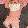 baby, infant, pink_clothing, headband, bib, socks, lying_down, carpet, blanket, cute, child, indoors, soft_lighting, portrait, small_heart_pattern, newborn, baby_girl, cozy, relaxed, adorable