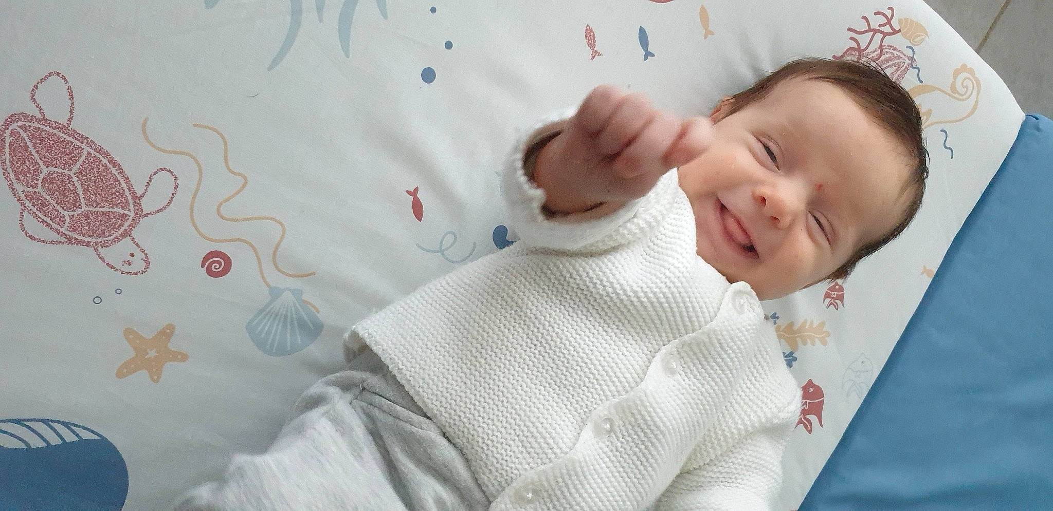 élise participe au concours pour gagner de l'argent avec cette photo : baby, baby_toddler_clothing, bed, bedding, child, collar, comfort, finger, gesture, happy, linens, pattern, person, product, room, skin, sleeve, smile, textile, thumb